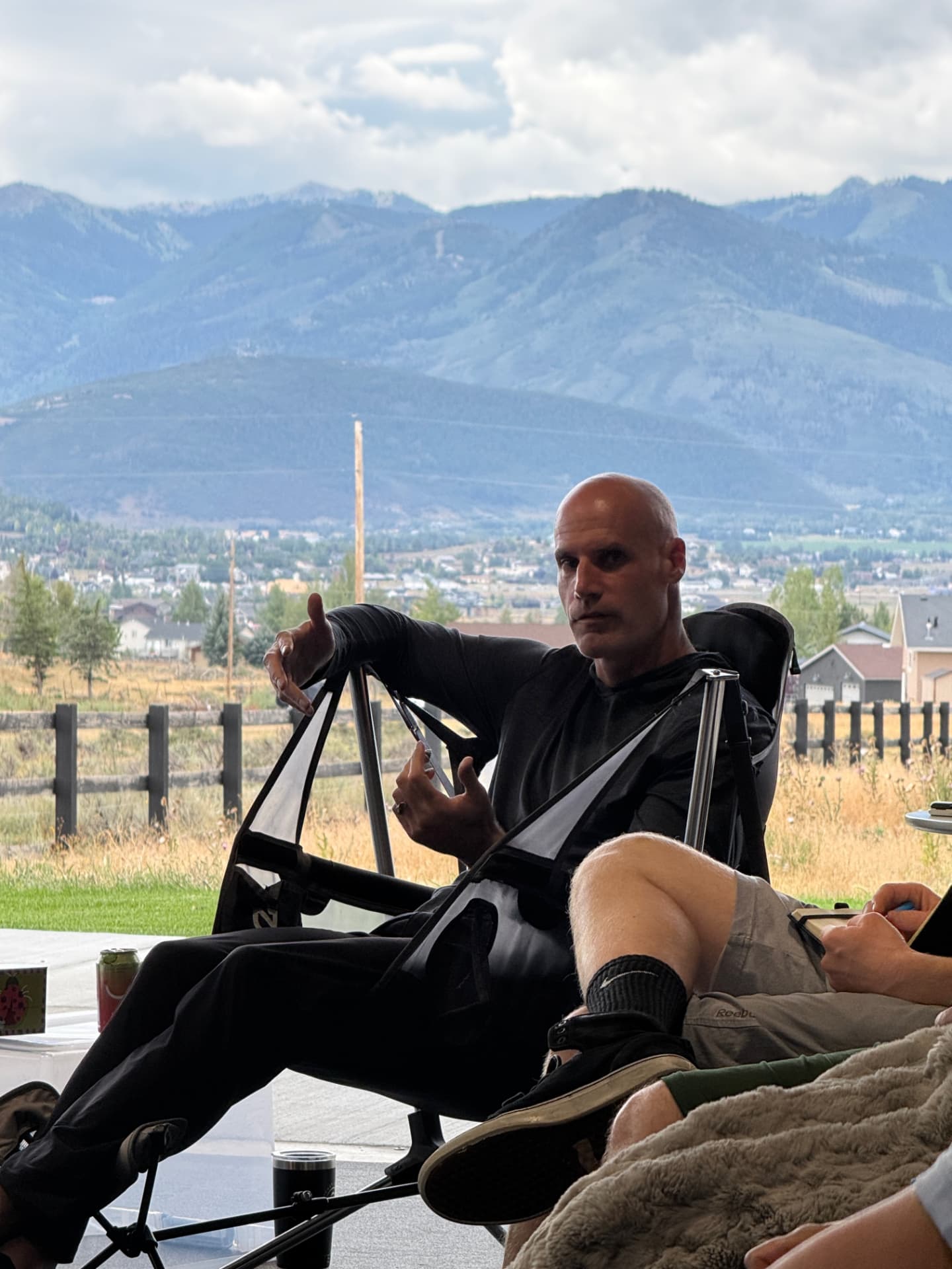 A facilitator speaking from a camp chair with a wide mountain valley in the background
