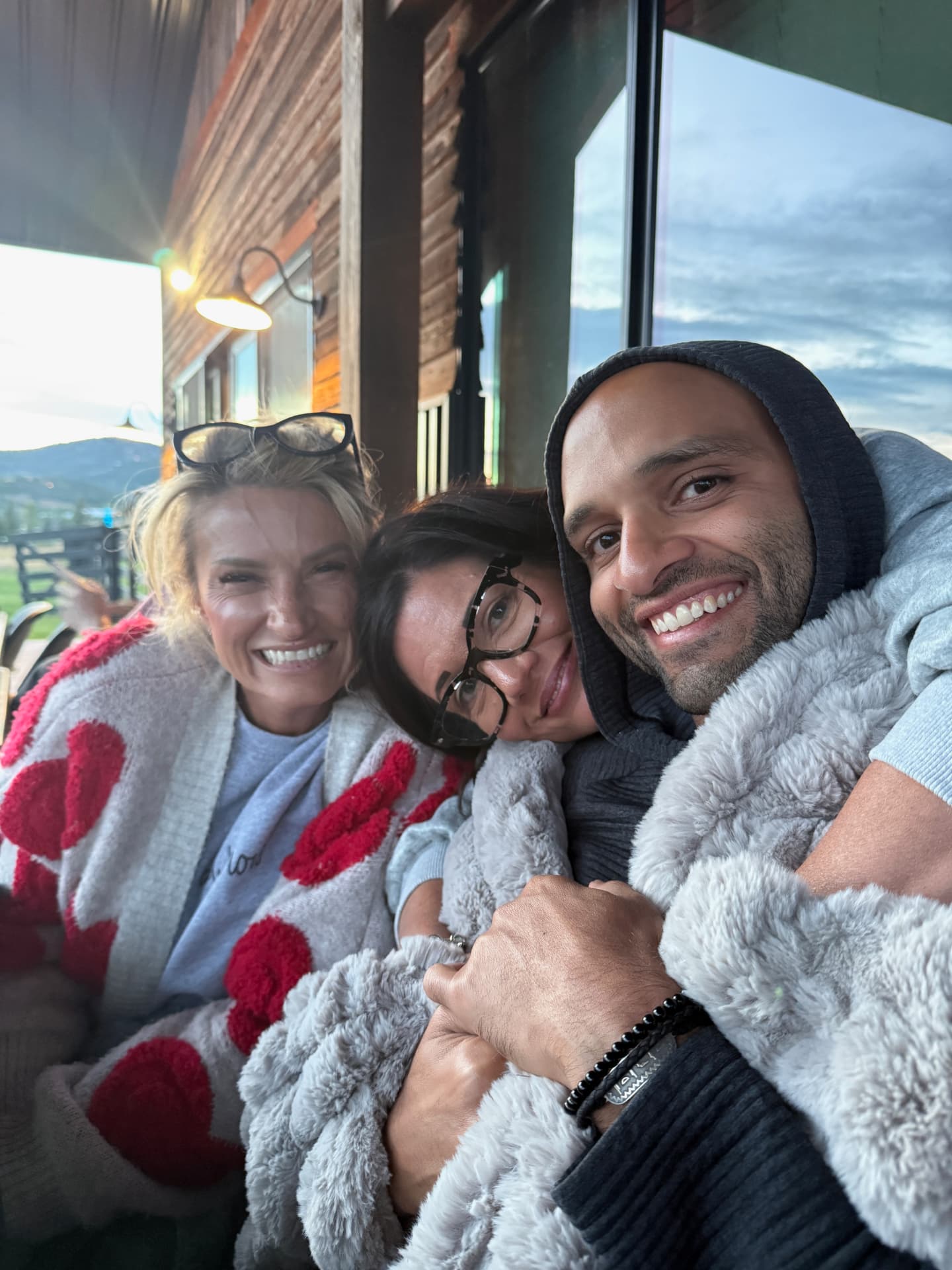 Three participants wrapped in blankets, leaning together and smiling at dusk